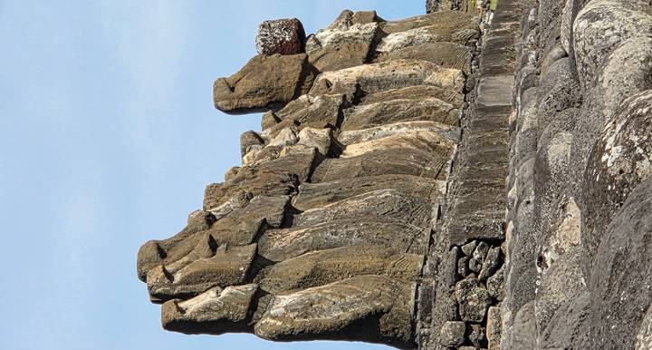Side view of a long row of iconic Moai stone statues standing on a stone platform under a blue sky