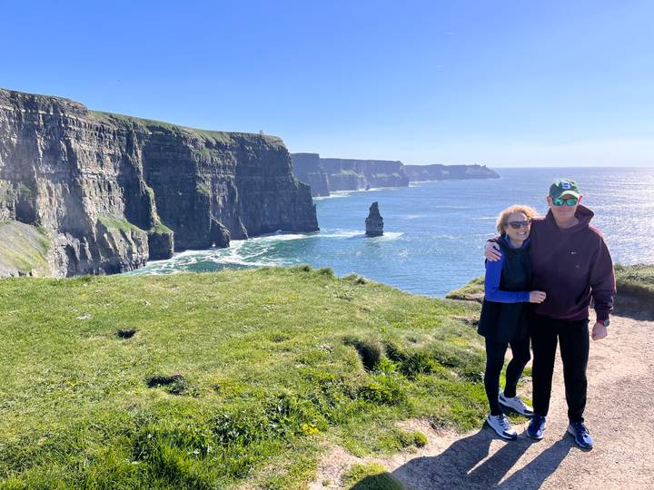 Smiling couple posing in front of the Cliffs of Moher with blue ocean behind them