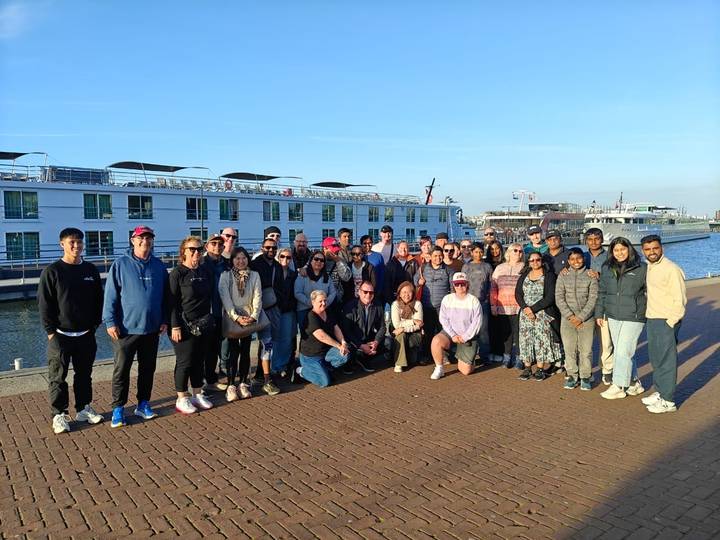 Tour group stands on dock beside river cruise ship under clear sky.