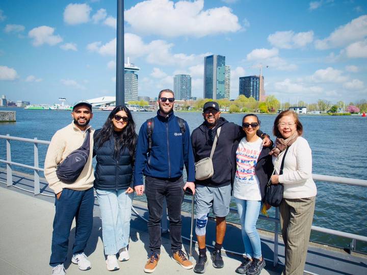 Small group pose by Amsterdam waterfront with modern skyline behind.