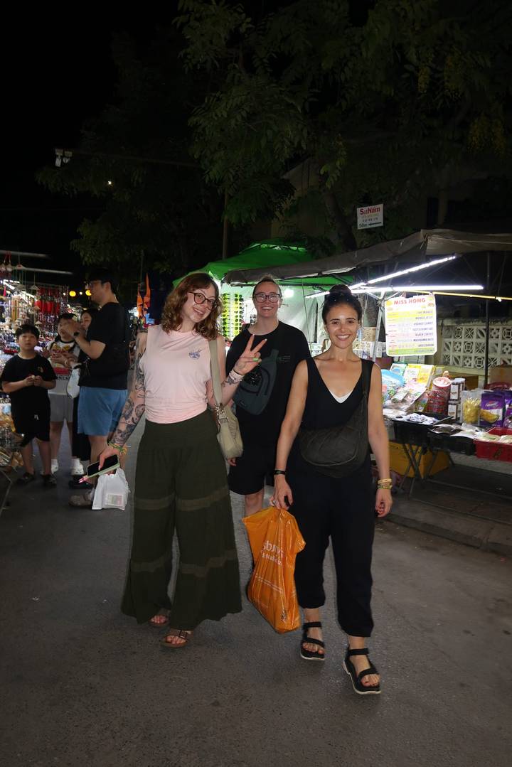 Travelers smile while browsing vibrant night market stalls.