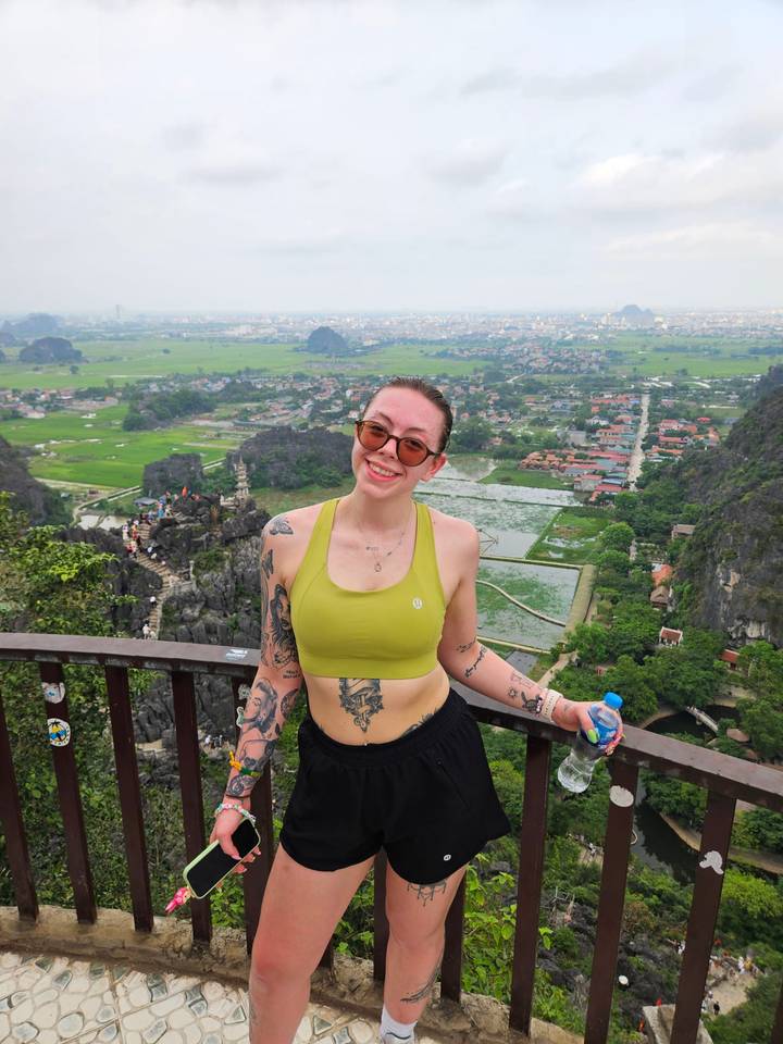 Young woman posing at a high scenic lookout over green rice fields, karst peaks and villages.