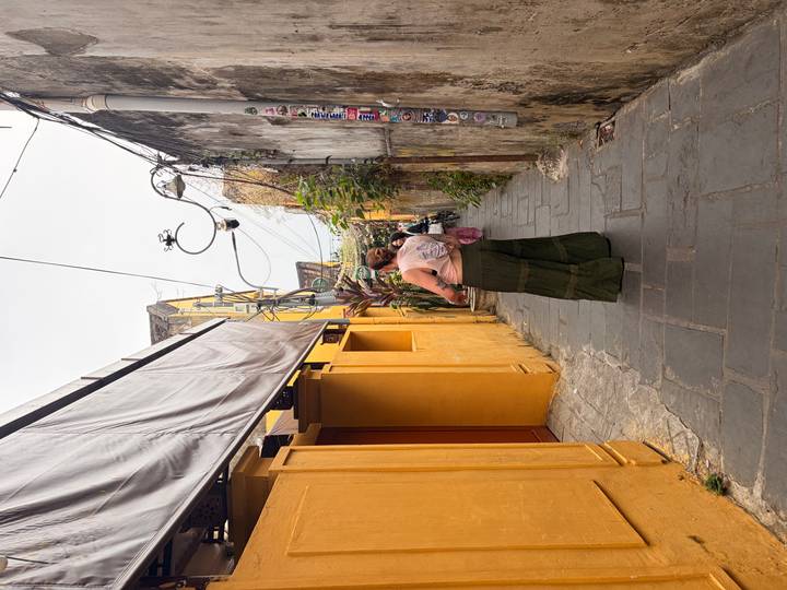 Back-view of a traveller walking through a narrow yellow alley of old-town buildings lined with wires and plants.