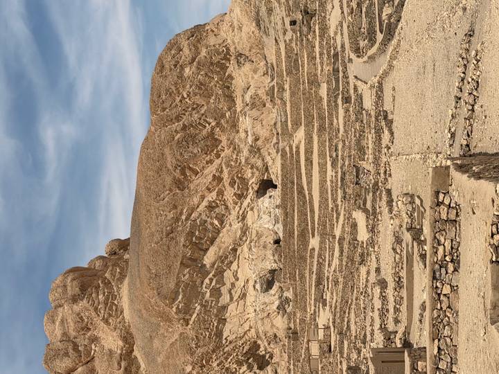 Rocky stepped ruins and barren hills under a partly cloudy sky in the Valley of the Kings.