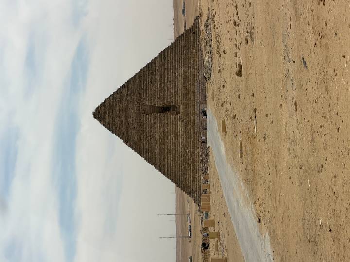 Isolated pyramid with a distinctive hole in its face rising from the desert under wispy clouds.