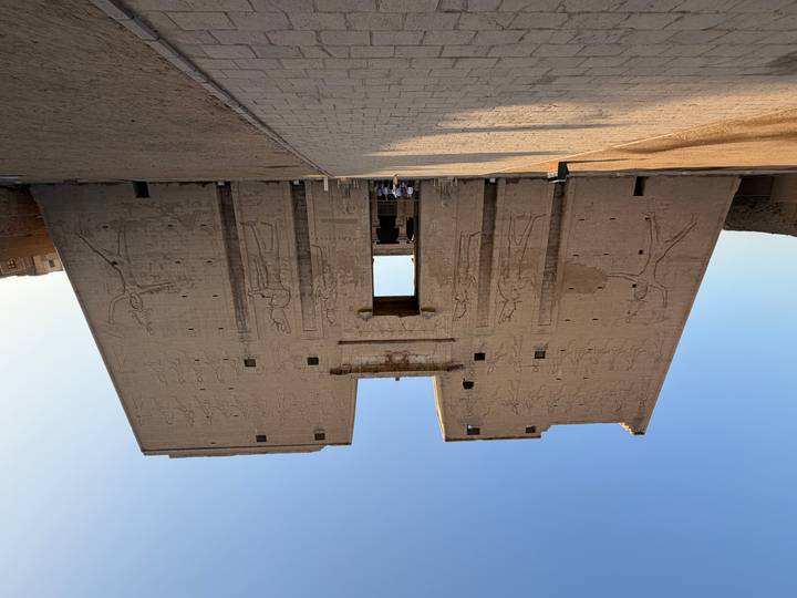 Front view of a massive pylon entrance covered with ancient Egyptian reliefs at a temple complex with tourists below.