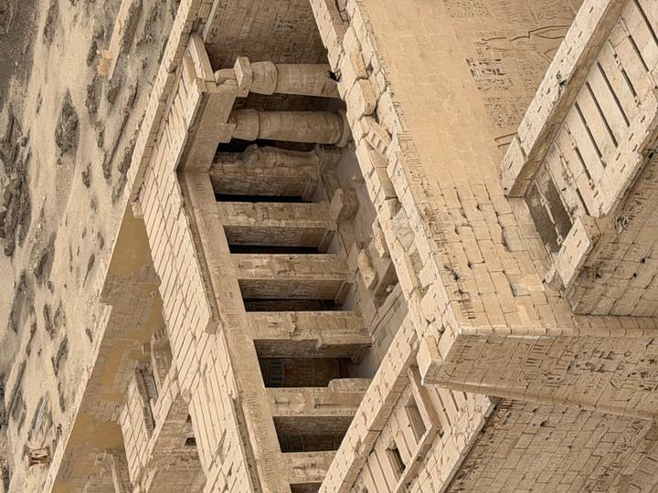 Close-up aerial angle of inner temple courtyard with carved columns and hieroglyphic walls in sandy tones.