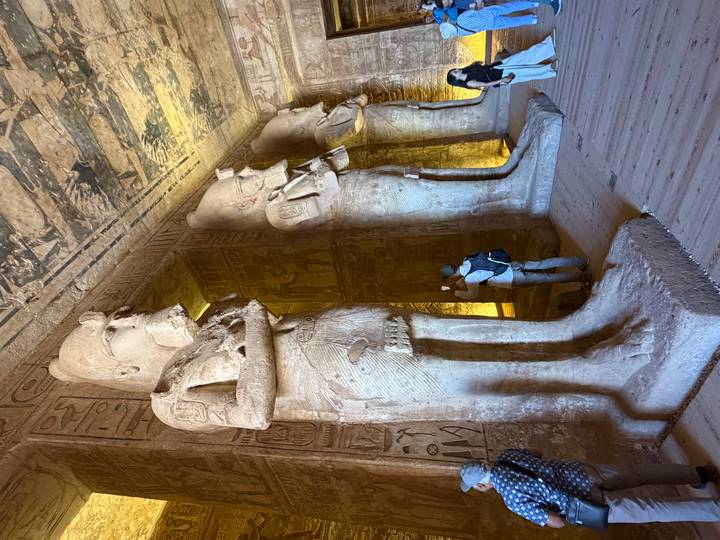 Interior of Abu Simbel temple with colossal standing statues carved into sandstone, visitors dwarfed by their size.