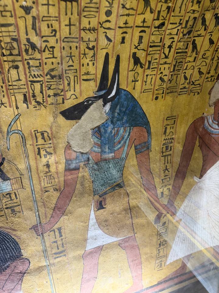 Detailed wall painting of the jackal-headed god Anubis with vivid colors and hieroglyphics in an ancient tomb.