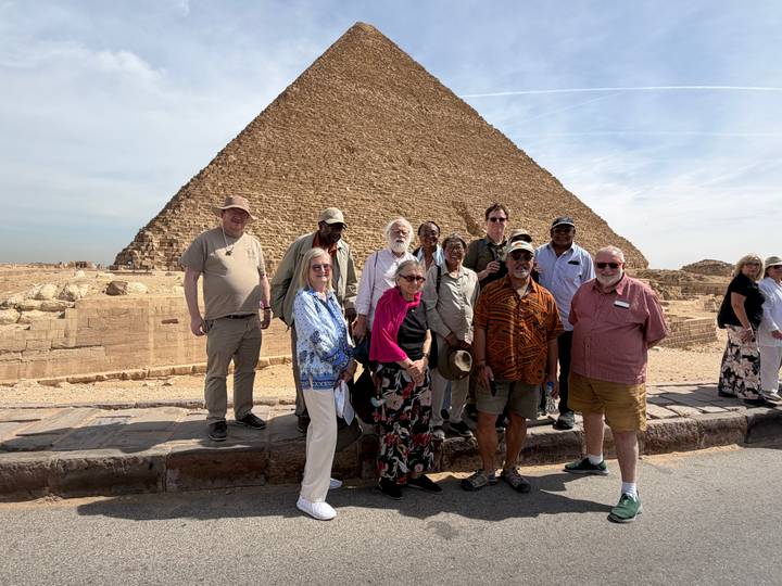 Tour group poses in front of one of the Giza pyramids on a bright day.