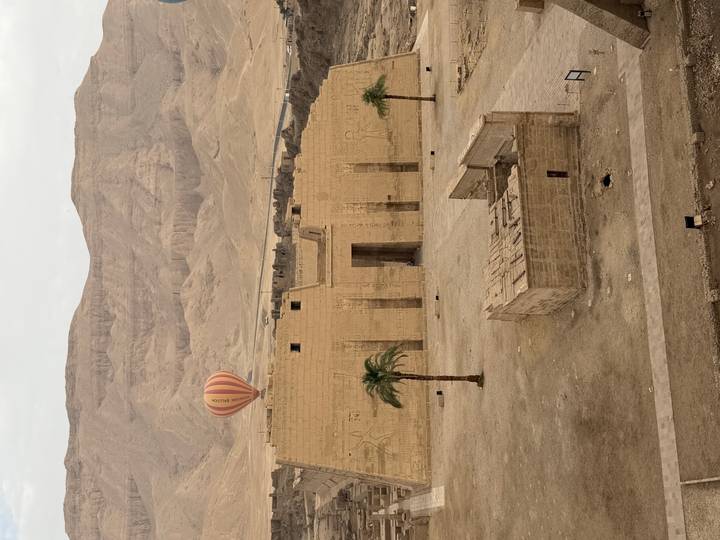 Temple complex sits beneath rugged desert mountains with a single hot-air balloon floating overhead.