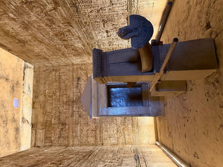 Dimly lit sanctuary room with ornate stone barque shrine and carved walls inside Edfu Temple.