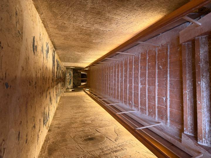 Long descending staircase lined with ancient wall carvings inside an Egyptian tomb, illuminated by warm lights.