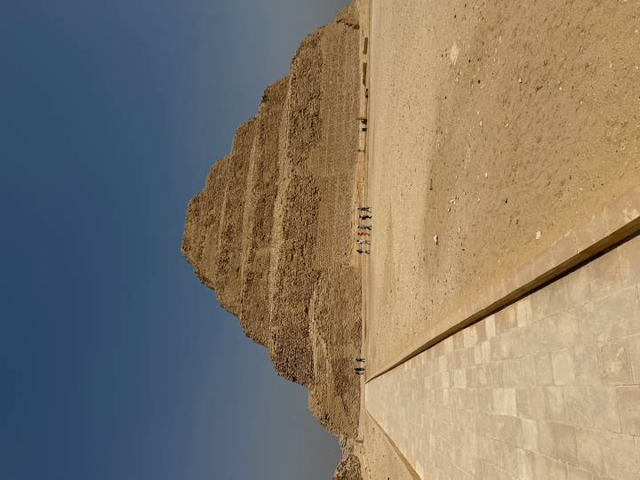 Wide view of the Step Pyramid of Djoser rising from the desert with a line of tiny visitors crossing the sandy forecourt.