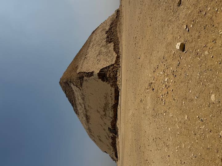 The Bent Pyramid shows its distinctive change in angle against a pale desert sky with rubble in the foreground.