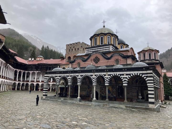 Striped black-and-white arcaded façade of Rila Monastery surrounded by forested mountains.