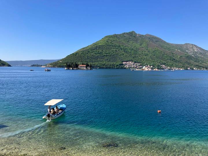 Serene blue bay with boat and green mountains; tiny church islands visible offshore.