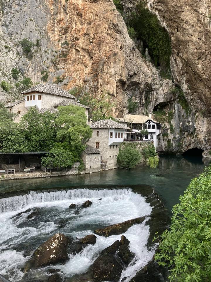 Historic dervish monastery complex beside cascading waterfall and lush greenery.