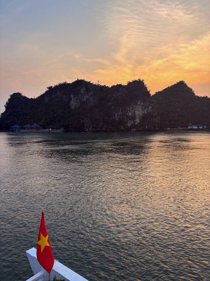Still waters of Halong Bay reflect limestone islands under pastel sunset sky.