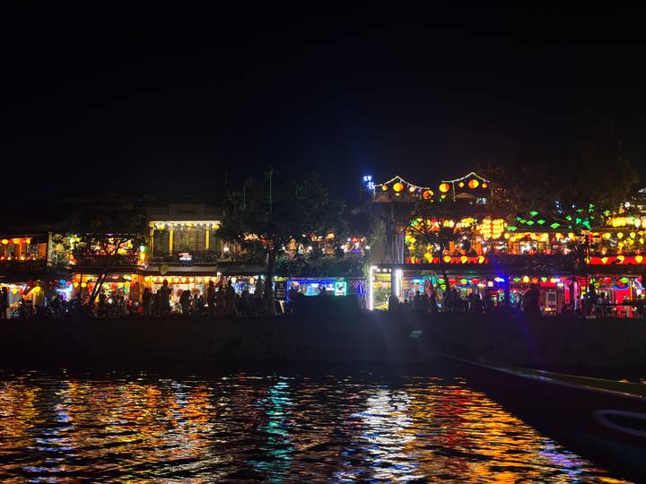 Riverside buildings in Hoi An ablaze with colorful lanterns reflecting on the water at night.