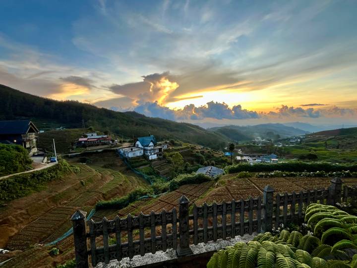 Golden-hour view of a hill village and patchwork farms under a dramatic sunset sky.