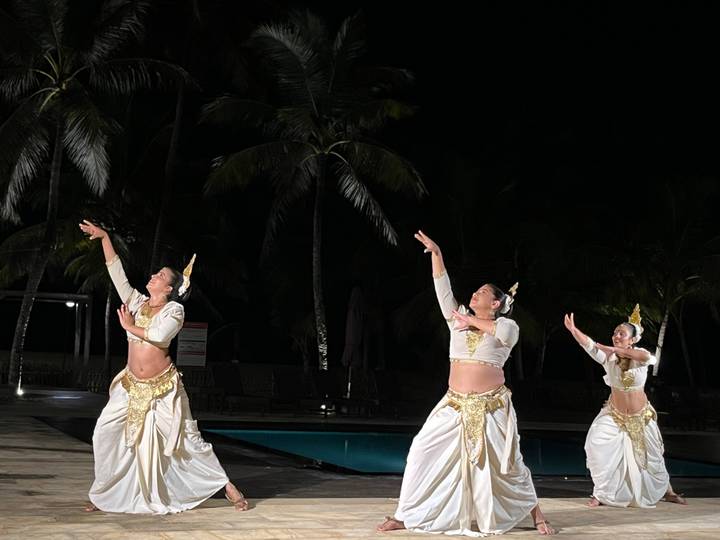 Three costumed Sri Lankan dancers perform by a pool at night.