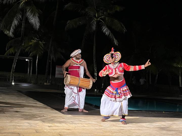 Drummer and masked dancer in traditional Sri Lankan attire performing at night.