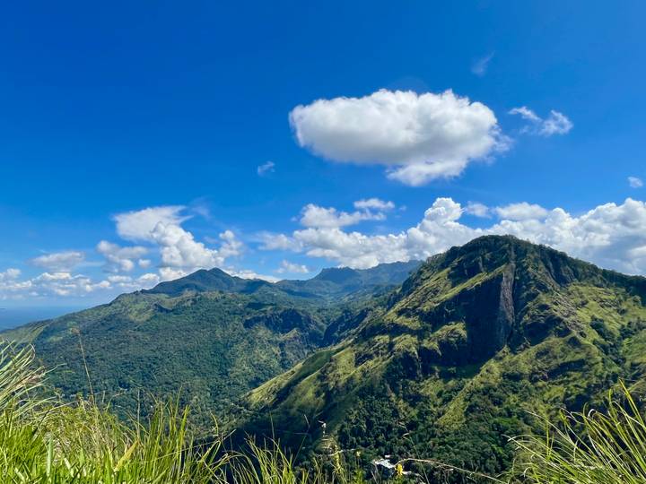 Panoramic view of lush green mountains beneath a bright blue sky with scattered clouds.