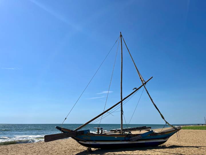 Traditional sailboat resting on a sandy tropical beach under a clear blue sky.
