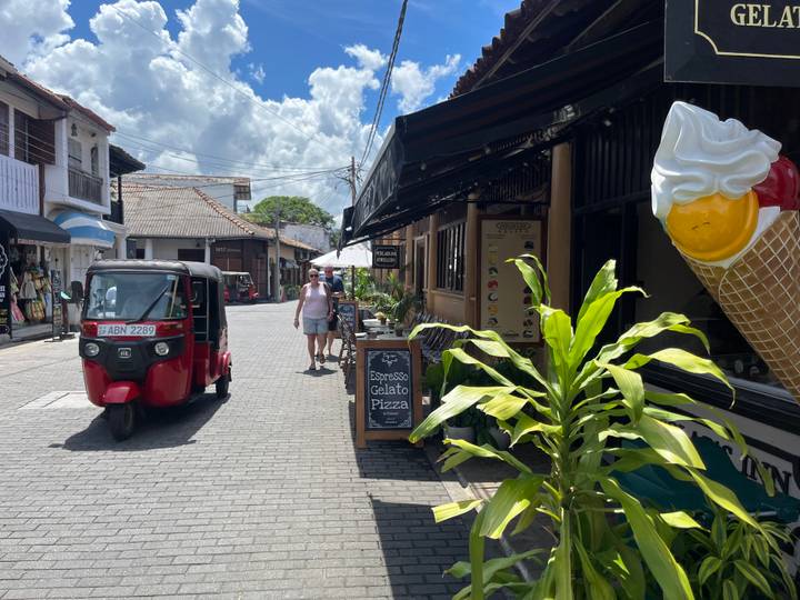 Cobblestone street in Galle Fort with tuk tuk, tourists, shops and a giant ice-cream cone sign.