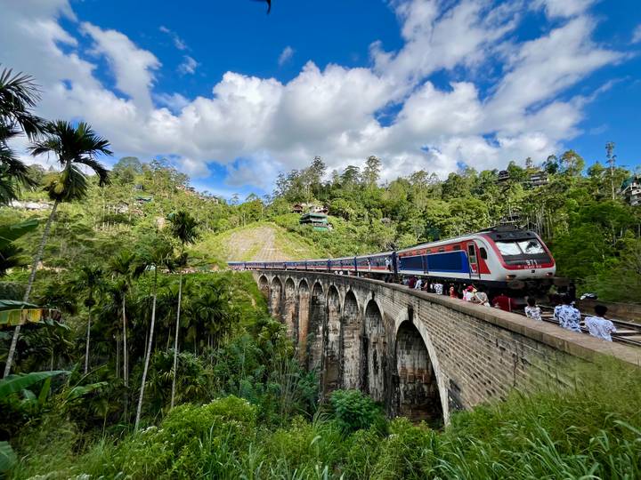 Passenger train crossing the iconic Nine Arches Bridge amid lush forest.
