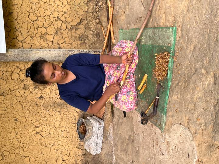Local woman seated on a mat preparing spices with traditional tools.
