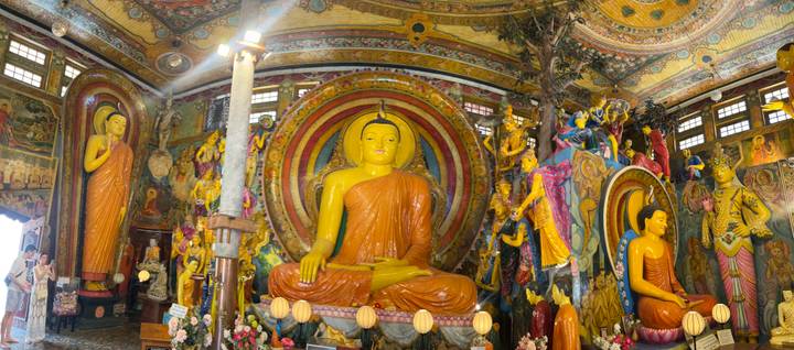 Vivid interior of a Buddhist temple dominated by a large seated Buddha and colourful murals.