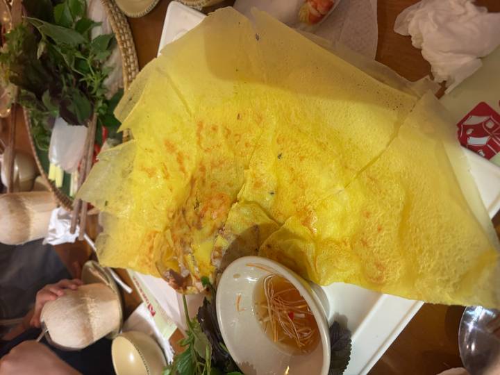 Large sizzling Vietnamese bánh xèo pancake served on a platter with herbs and dipping sauce.