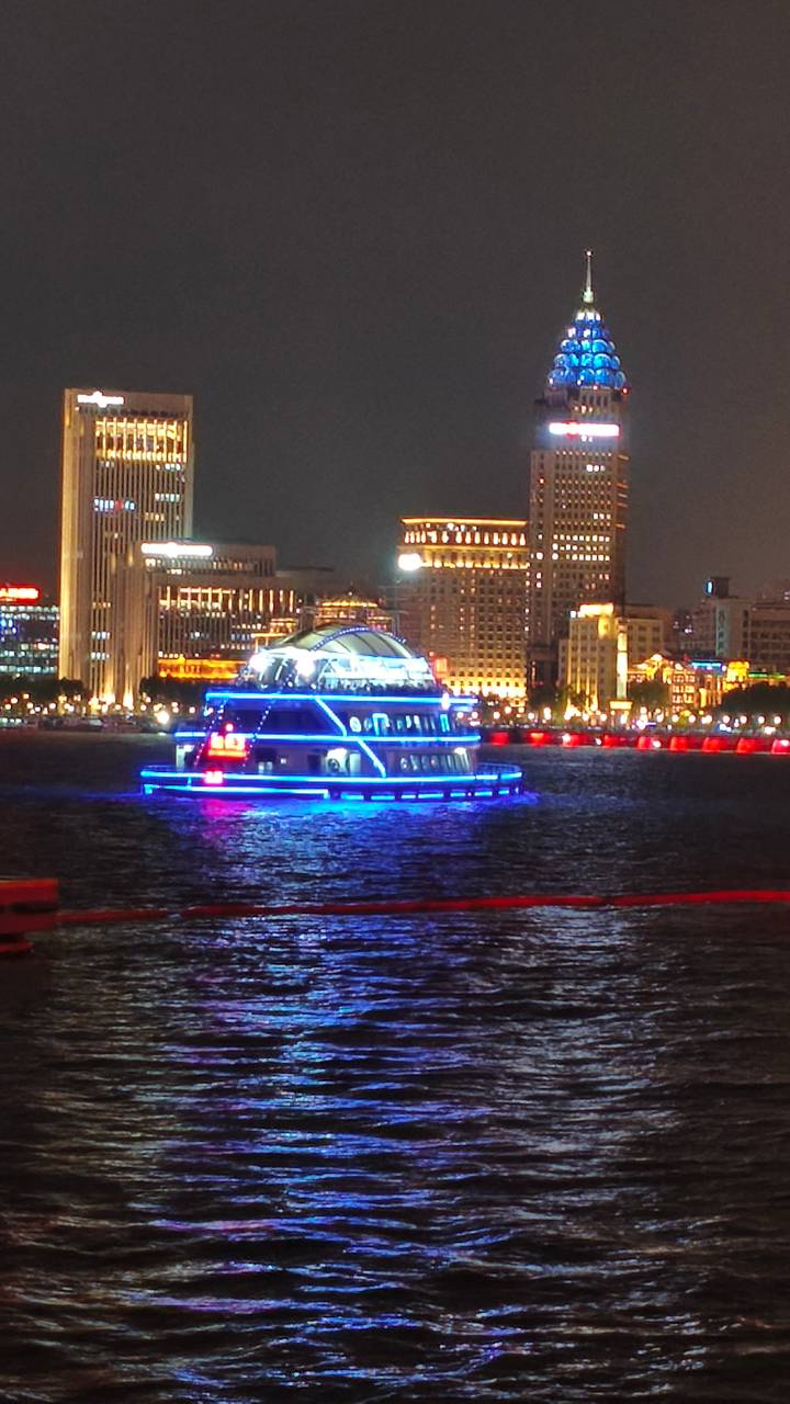 Neon-lit sightseeing boat gliding along a river against Shanghai’s illuminated skyline.