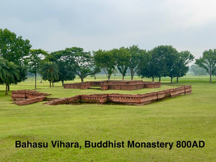 Low brick ruins of an ancient Buddhist monastery set in a broad green lawn.