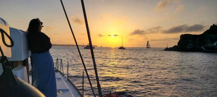 Woman on a catamaran gazing at a golden Aegean sunset dotted with sailboats