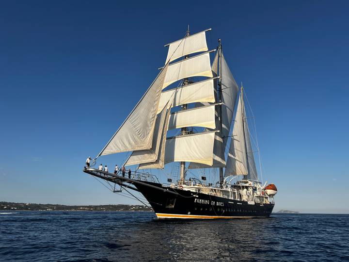 Close-up angle of tall ship with crew on bowsprit preparing sails
