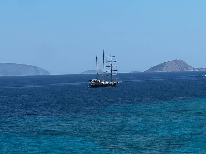 Distant view of a masted yacht anchored in deep blue Aegean waters with islands behind