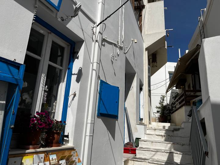 Narrow Greek alley with whitewashed walls, blue shutters and bright flower pots under clear sky