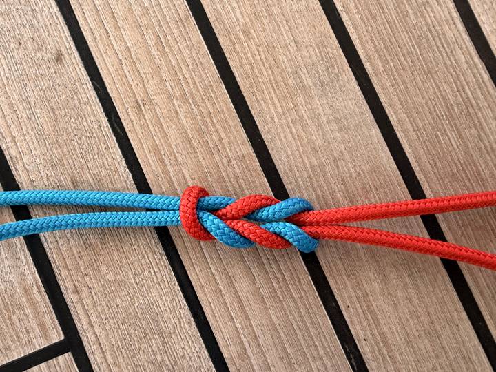 Close-up of red and blue rope neatly tied in a decorative knot on teak decking