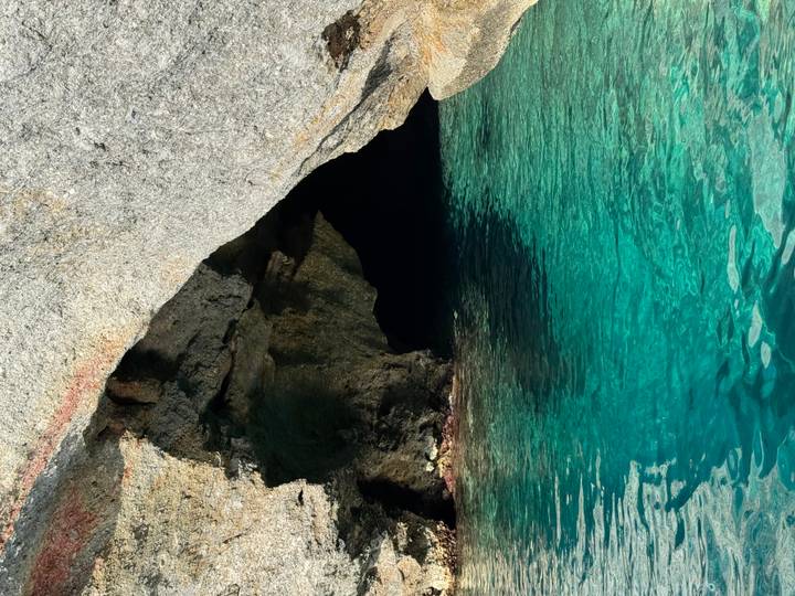 Turquoise water at the mouth of a rocky sea cave glinting in sunlight