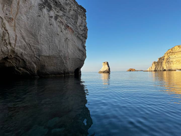 Serene coastal scene with towering rock cliffs and calm reflective water at golden hour
