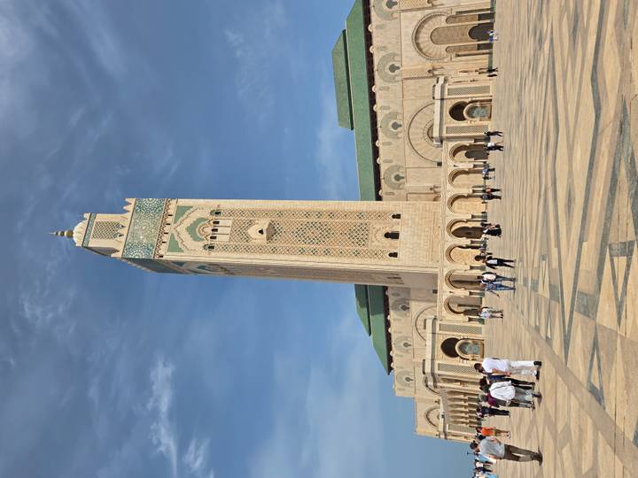 Imposing Hassan II Mosque minaret towers over a spacious marble plaza with scattered visitors.