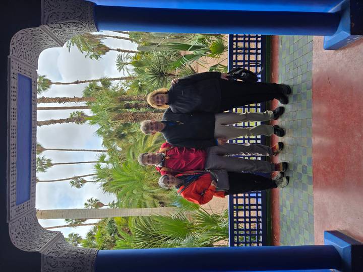 Four travellers stand in the lush Majorelle Garden framed by palm trees and colourful tiles.