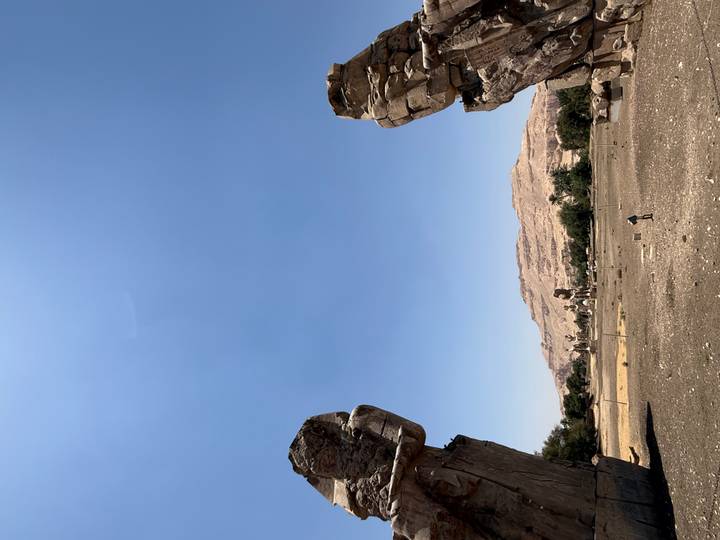 Colossi of Memnon statues frame a distant barren hill under a cloudless Egyptian sky.