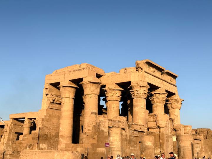 Golden-lit columns and reliefs of Kom Ombo Temple glowing against a clear evening sky.