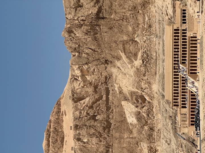 Temple of Hatshepsut nestled beneath towering limestone cliffs under a clear blue sky.