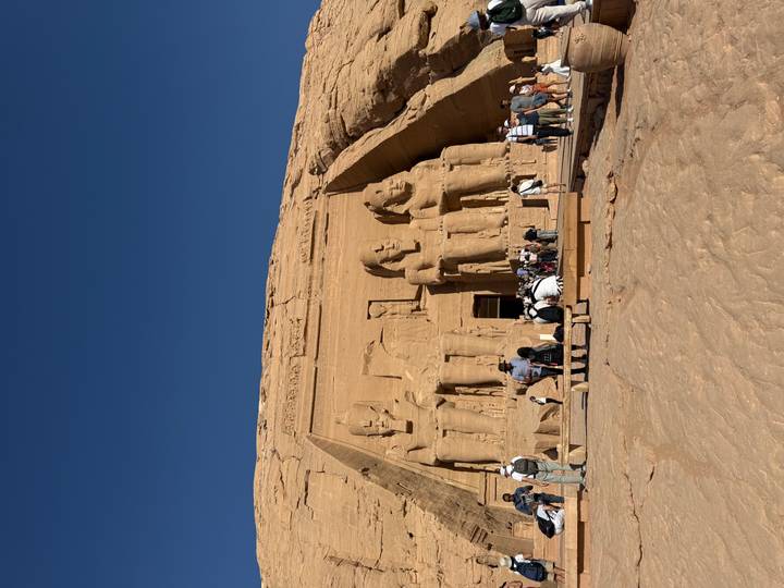 The colossal seated statues of Abu Simbel with many visitors exploring the forecourt under a deep blue sky.