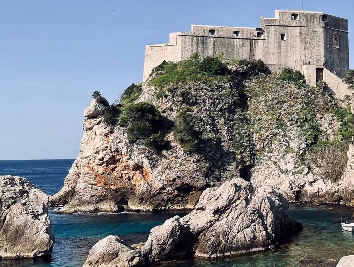 Stone fortification of Dubrovnik perched on a rugged cliff above the deep-blue Adriatic Sea.